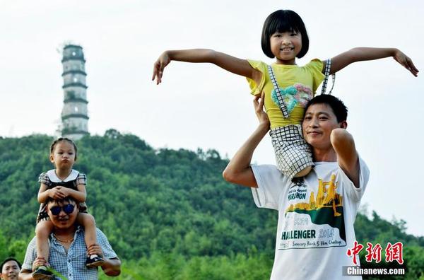 图为8月25日，“无腿女孩”蒋张子怡坐在父亲的肩上，开心用“飞翔”的双手，与当地坚挺400多年的半边古塔媲美。卓忠伟 摄