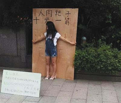 　杭州武林广场一女孩站在一块大木板前头，木板上写有“人肉靶子，十元一箭”字样。