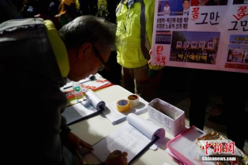 10月29日晚，近两万名韩国民众及民间团体人士在首尔市中心举行烛光集会，谴责“亲信干政事件”给韩国社会带来的不良影响，要求总统朴槿惠对此事负责。图为民众在集会现场写下请愿书，要求查明事情真相。<a target='_blank' href='http://www.chinanews.com/'>中新社</a>记者 吴旭 摄