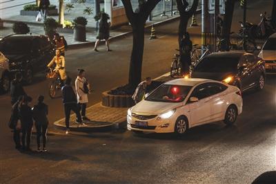 4月20日，三里屯太古里街边，一辆亮着红色条灯的黑车驶过，路边一位男子正在询问司机价钱。新京报记者 彭子洋 摄