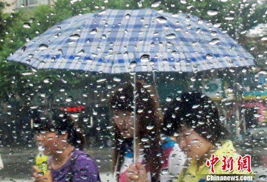 6月28日，隔着滴满雨珠的车窗，打着雨伞的市民在南京街头经过。泱波　摄