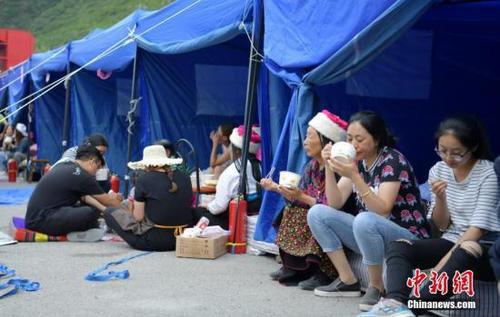 8月10日，四川九寨沟“8.8”地震震源中心附近的临时安置点，受灾村民在帐篷边吃饭。中新社记者 刘忠俊 摄