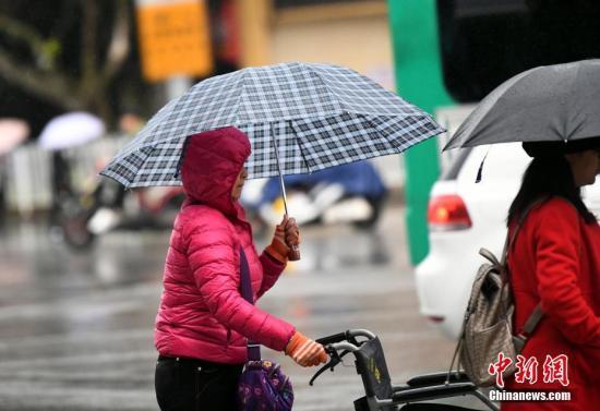 资料图：昆明市区里身着羽绒服冒雨赶路的民众。 中新社记者 李进红 摄