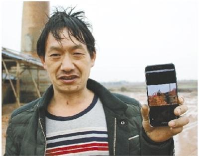 1月27日，严国有向记者展示他手机上的照片——老板用来抵工资的大量红砖。现在，他身后堆放红砖的地方已经成了空地。