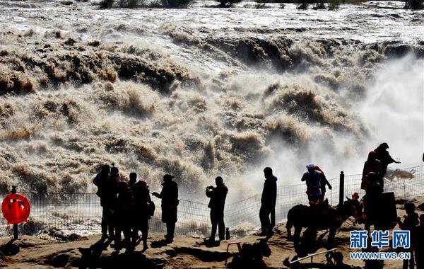 10月11日，游客在壶口瀑布参观。 近日，位于晋陕大峡谷的黄河壶口瀑布水量持续增大，主副瀑布连成数百米的大瀑布，形成“水岸齐平”景观。