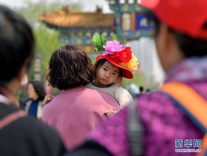 4月8日，一名头戴“牡丹”花帽的小游客和家人一起游园。