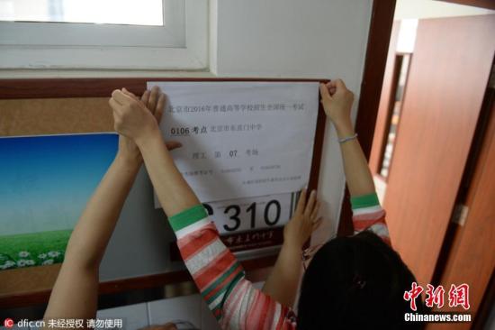 2016年6月3日，北京，东直门中学考点，教室外已贴上了统一印制的考场信息，上面显示着考点编号、名称及具体的考场号。教室内设置了约30个考生座位，座位与座位之间的距离约为80厘米以上。两位考务老师手持一叠写有学生姓名、准考证号的桌签走进教室，按考场座位安排表逐一贴在桌子上。随后，一位老师在黑板上写下了当科开考的科目、考试时间和试卷份数。图片来源：东方IC 版权作品 请勿转载