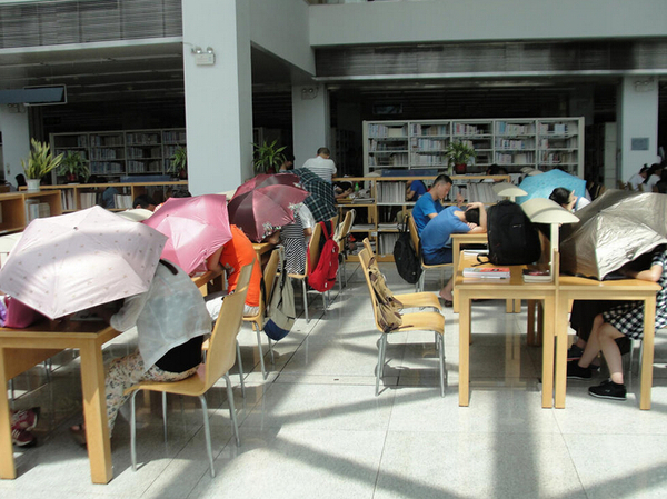图书馆内撑伞读书的民众。