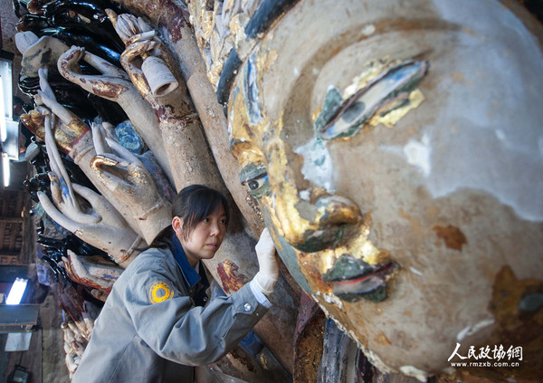2014年3月18日，一名大足石刻千手观音造像修复人员在检查揭取金箔后露出的主尊像石质胎体。