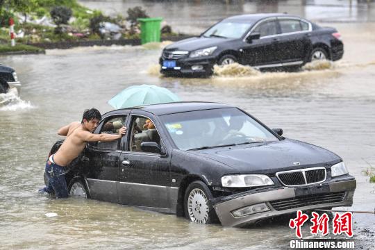 6月13日，惠州惠东县新平大道上，市民在雨中推行抛锚的车辆。　陈骥旻 摄