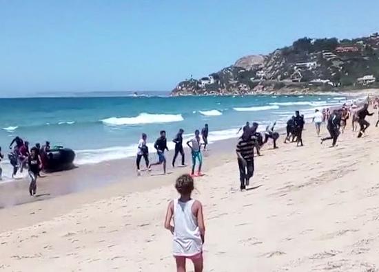 视频截图：8月9日，西班牙南部海滨，一名妇女注视着非洲非法移民冲上海滩。（新华/美联）