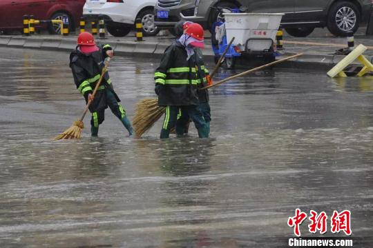 图为环卫工人们冒雨清扫路面。　邓建青 摄