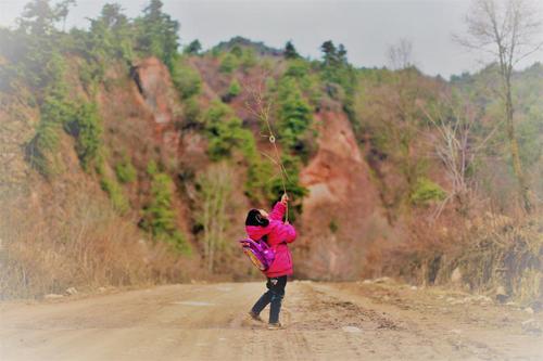 放学路上，乐乐拿着树枝独自玩耍，她的父亲在北京打工，母亲在一次洪水中去世。 （刘飞越 摄于甘肃陇南）