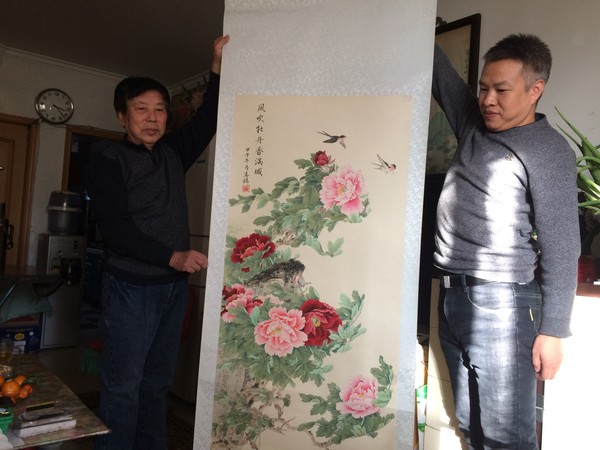 图为北京工艺美术大师阮春麟（图左）与保健中医专家王磊在家中展示自己的中国画作《风吹牡丹香满城》。