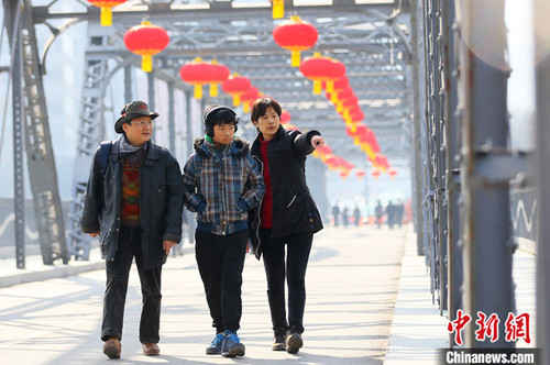 2021年春节期间，台湾商人杜书亿一家三口走过挂满火红灯笼的兰州中山铁桥。 中新社记者 高展 摄